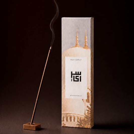 Oud incense stick burning in a holder beside an Oud Fakhama box
